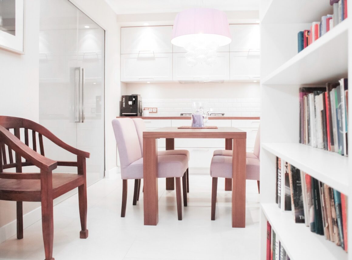 biała kuchnia z drewnianym stołem i różowymi krzesłami