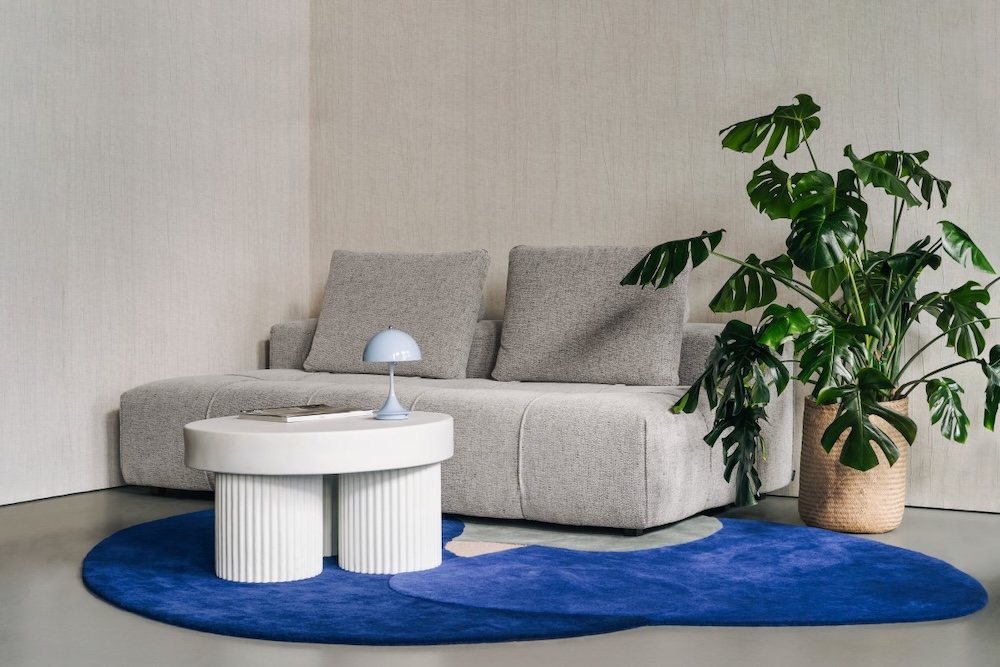 szara sofa i biały stolik na granatowym dywanie szara sofa pod ścianą z białym geometrycznym stolikiem kawowym