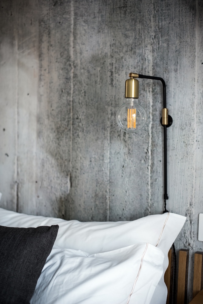 ściana z szarego cementu za łóżkiem w sypialni  cementowa ściana z czarną lampą w sypialni za łóżkiem