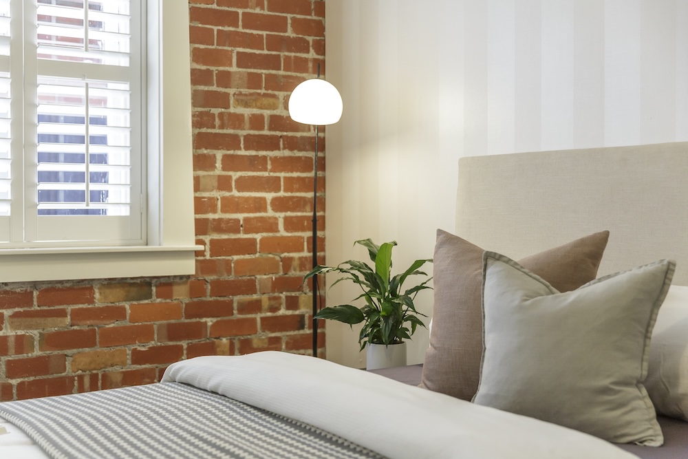 jasna sypialnia z oknem i ceglaną ścianą  sypialnia z jedną ścianą z czerwonej cegły